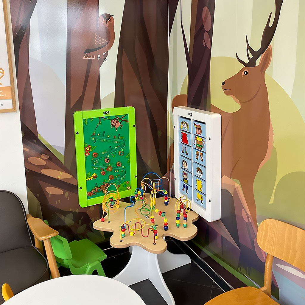 Kinderhoek met wandspelpanelen en kralentafel in een wachtruimte met bosdierenmuurprint. Ontworpen om kinderen op een speelse manier bezig te houden terwijl ouders ontspannen.