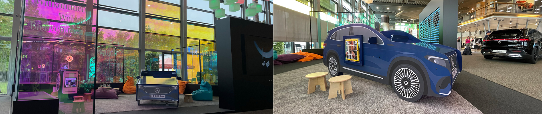 Kinderhoek in Mercedes-Benz showroom met interactieve speelobjecten, waaronder een blauw Mercedes-auto speelmeubel met wandspel, kleurrijke zitzakken en speeltafels, omgeven door grote glazen ramen en modern interieur.