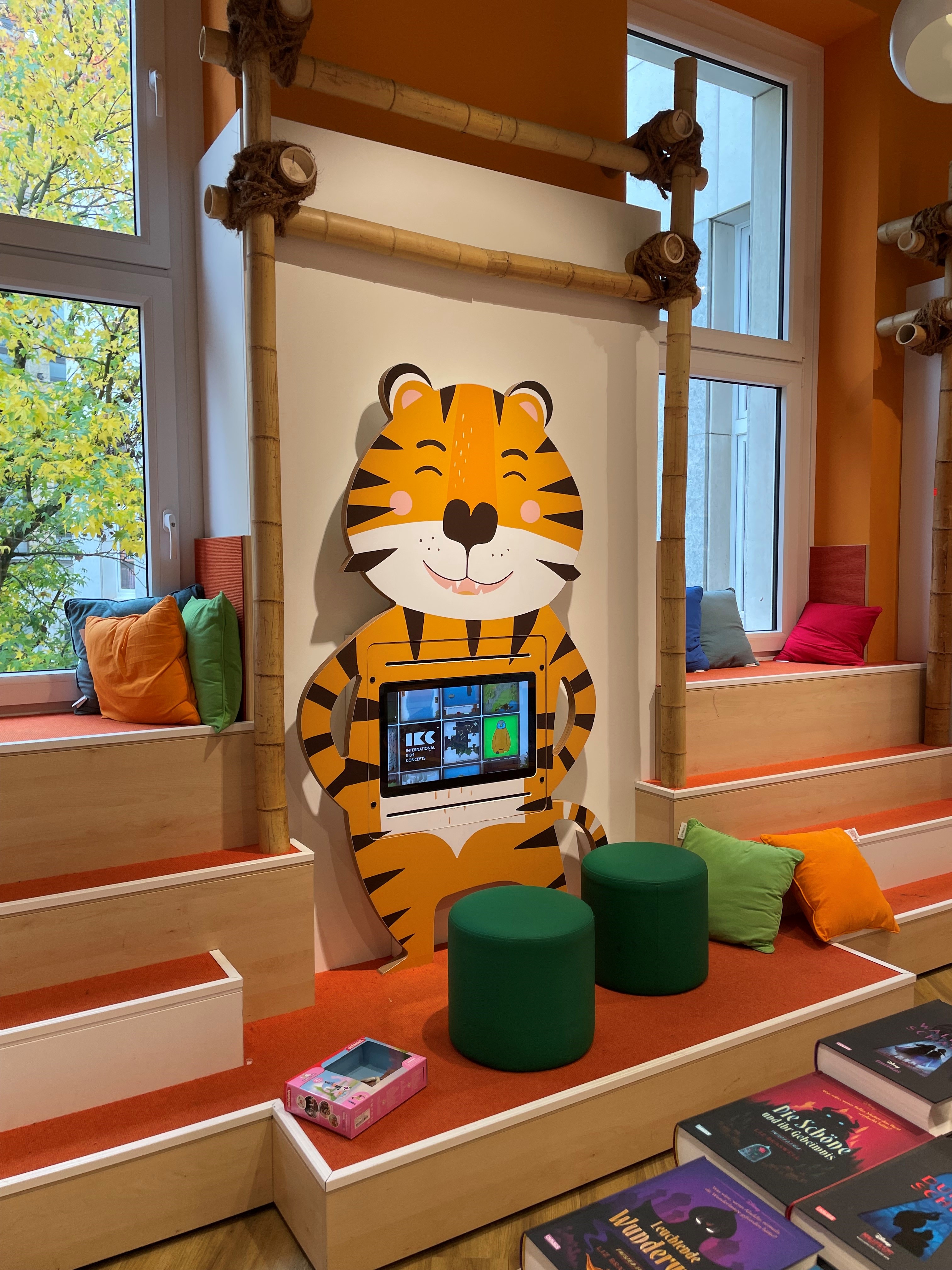 Espace enfants coloré avec un écran interactif intégré dans une borne en forme de tigre, installé dans la librairie Thalia à Krefeld.
